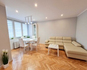 Un salon moderne avec un canapé beige, une table à manger blanche avec des chaises et une petite table blanche.