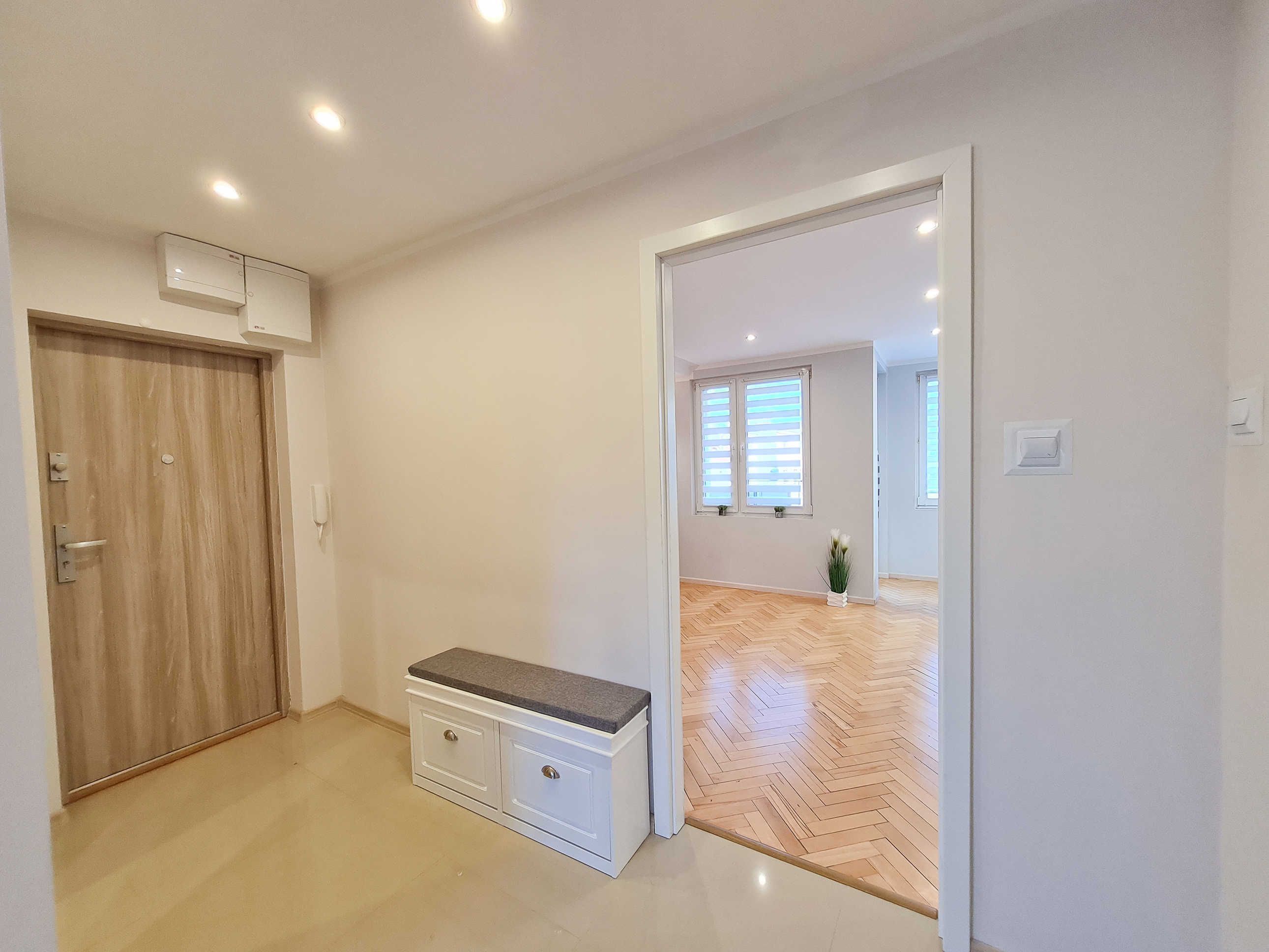 Ein Zimmer mit Holzboden, einer weißen Bank, einer Tür und einem Fenster mit Jalousien.