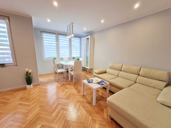 Una sala moderna con un sofá color beige, una mesita blanca pequeña y un comedor con una mesa redonda y sillas.