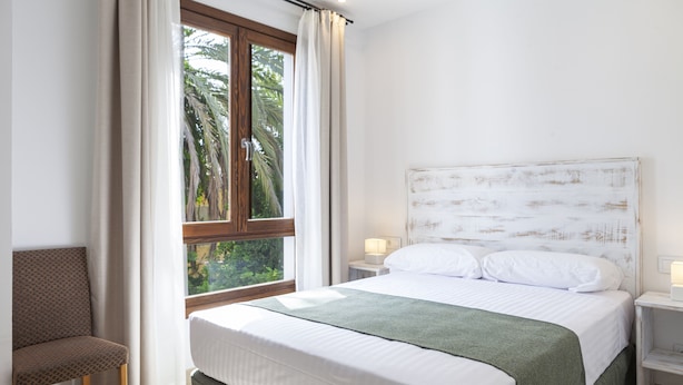 A bedroom with a large bed, two bedside tables, a chair, and a window with curtains. - Ad Hoc Vitae Retreats & Health - Adults Only (Beniarbeig)