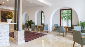 A spacious lobby with a high ceiling, a central seating area with chairs and a table, a decorative pillar, and a large window with a view of greenery. - Ad Hoc Vitae Retreats & Health - Adults Only (Beniarbeig)