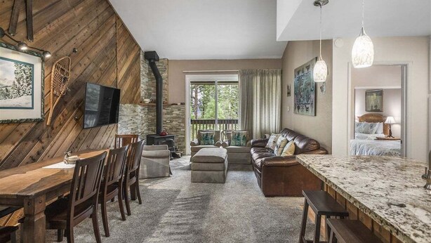 A cozy living room with a fireplace, a stone wall, a large window, and a bar area. - Crestview 30: Free EV Charger, Walk to The Village (Mammoth Lakes)