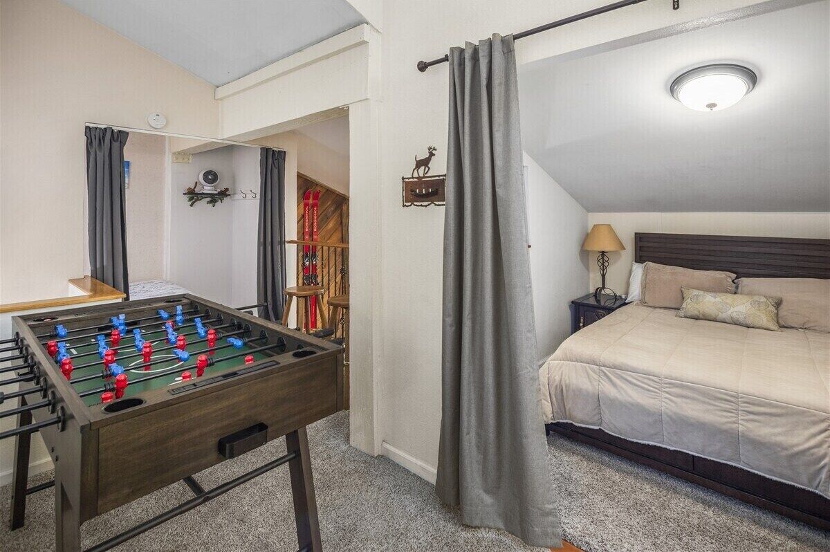 A room with a bed, a foosball table, a lamp, and a ceiling light.