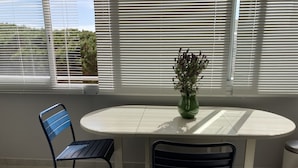 Et værelse med et rundt bord, to stole, en grøn vase med blomster og et vindue med skodder.