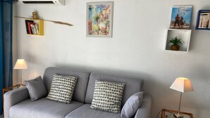 En grå sofa med mønstrede puder, to sengeborde med lamper, et bogskab fyldt med bøger og indrammede kunstværker på væggen.