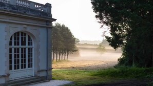 A building with a large arched window and a door, surrounded by trees and a foggy field. - Château la Gauchetiere Avec Piscine (Chailloué)