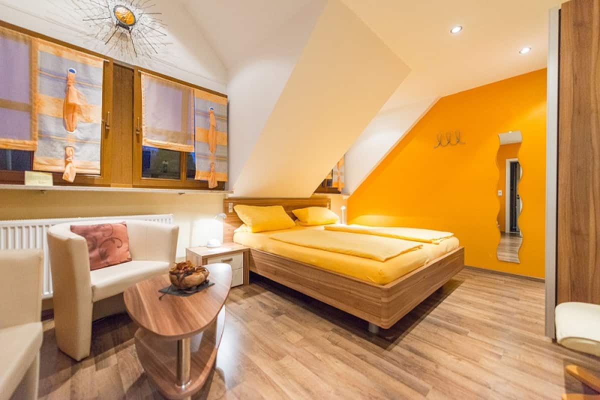 A modern bedroom with a bed, a sofa, a small table, and a radiator.
