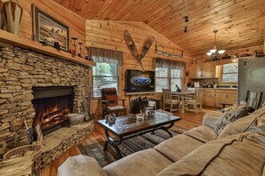 Un intérieur de chalet chaleureux avec une cheminée en pierre, des murs en bois, un coin repas et une cuisine.