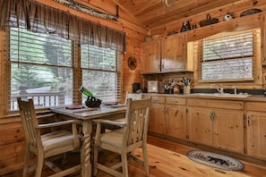 L’intérieur d’un chalet en bois comprend une table à manger, des chaises, une cuisine avec des meubles en bois et de grandes fenêtres.