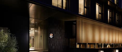 Une entrée d’hôtel moderne avec une porte en verre, un comptoir d’accueil et un décor composé de panneaux en bois verticaux.