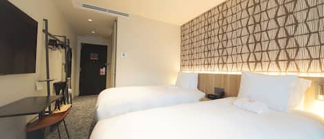 Habitación de hotel con dos camas, un escritorio y una silla. Hay un televisor montado en la pared y una puerta que da a otra habitación.