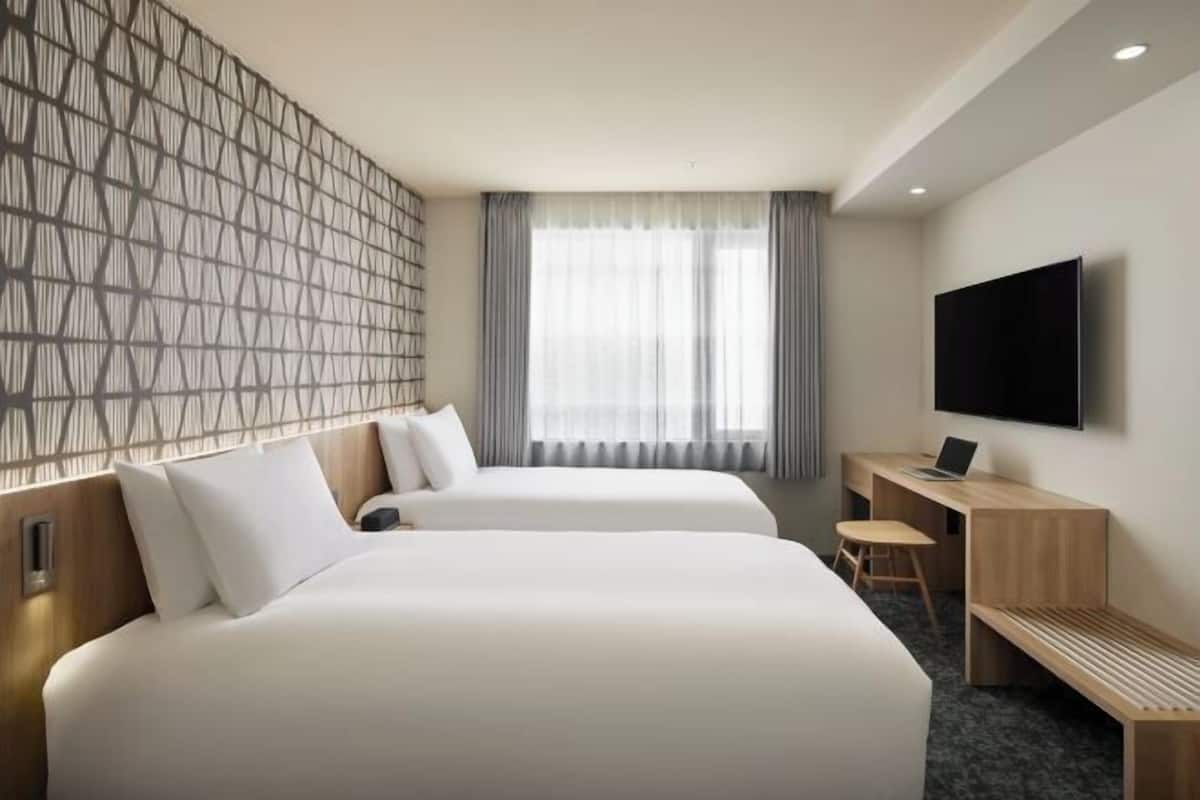 Une chambre d’hôtel avec deux lits, un bureau avec un ordinateur portable, une télévision et une fenêtre avec des rideaux.