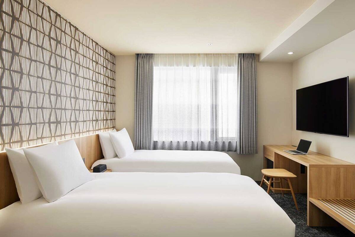 Une chambre d’hôtel avec deux lits, un bureau, une chaise, une télévision et une fenêtre avec des rideaux.