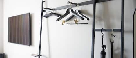 A modern room with a black metal rack holding black and white hangers, a black exercise bench, and a mounted TV on the wall.