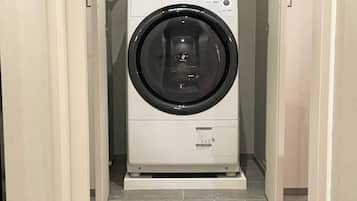 A compact, white front-loading washing machine in a narrow hallway with tiled flooring.