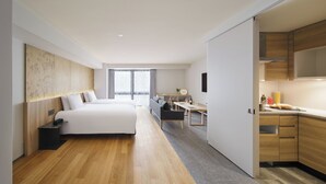 A modern hotel room with a large bed, a desk, and a kitchenette.