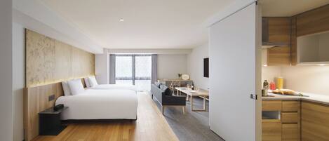 A modern hotel room with a large bed, a desk, and a kitchenette.