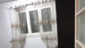 Et soveværelse med seng, gardiner ved vinduet, en dør og et tæppe med mønster.
