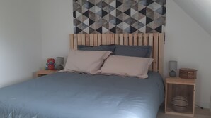 Ein Schlafzimmer mit einem Holz-Kopfteil, einem Bett mit blauer Bettwäsche, zwei Kissen, einem Nachttisch mit Lampe und einer Wanddekoration.