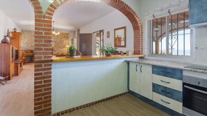 A kitchen with a brick archway, wooden cabinets, and a view of the sea. - Cortijo Tomé Solset (Torrox)