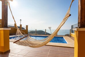 Una hamaca en una terraza con baldosas, una piscina y vistas al mar.