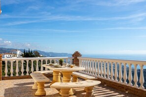 A terrace with a round table and benches, a white balustrade, and a scenic view of the sea and mountains. - Villa Olympo by Solset (Torrox)