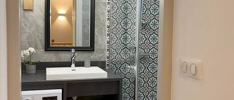 A modern bathroom with a built-in washing machine, a sink with a mirror, and patterned tiles.