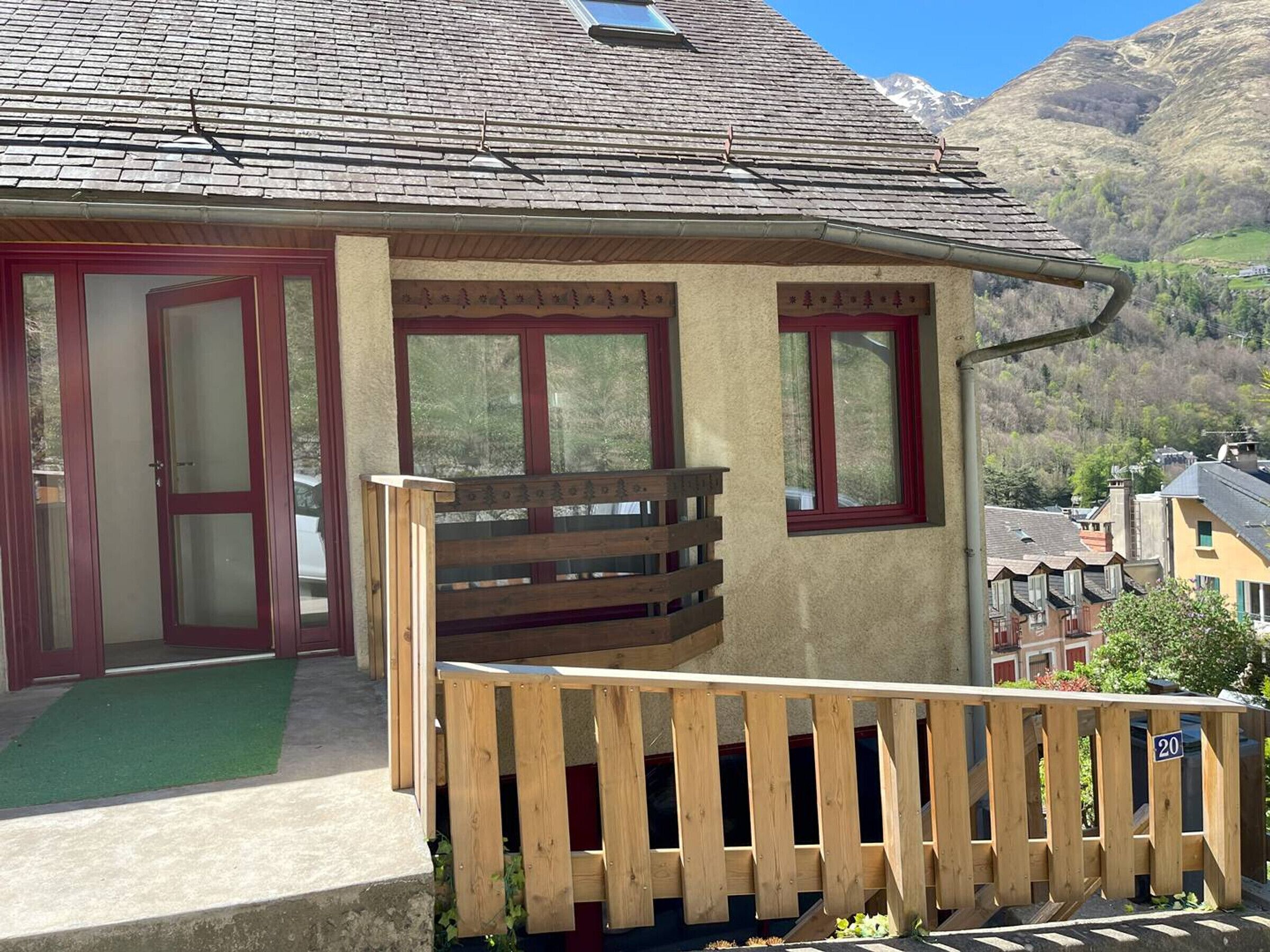 A building with a wooden balcony and red-framed windows, set against a mountainous backdrop.