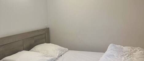 A bed with white bedding and pillows, a wooden headboard, and a wall-mounted light fixture.