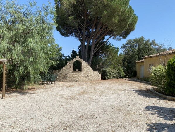 A courtyard with a stone staircase leading to a small arched entrance, surrounded by trees and a building with a tiled roof.
