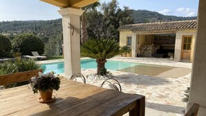 Taula de fusta amb una planta en test, una piscina i un edifici amb teulada de rajola.