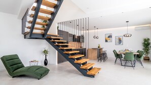 A modern interior with a spiral staircase, a green lounge chair, a dining area with a table and chairs, and a kitchen in the background. - Villa Top Hill,heated pool,Jacuzzi,Sauna,5 en-suite bedrooms,Media room (Tugare)