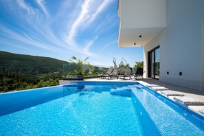 A modern outdoor swimming pool with clear blue water, surrounded by lounge chairs and a white building with large windows. - Villa Top Hill,heated pool,Jacuzzi,Sauna,5 en-suite bedrooms,Media room (Tugare)