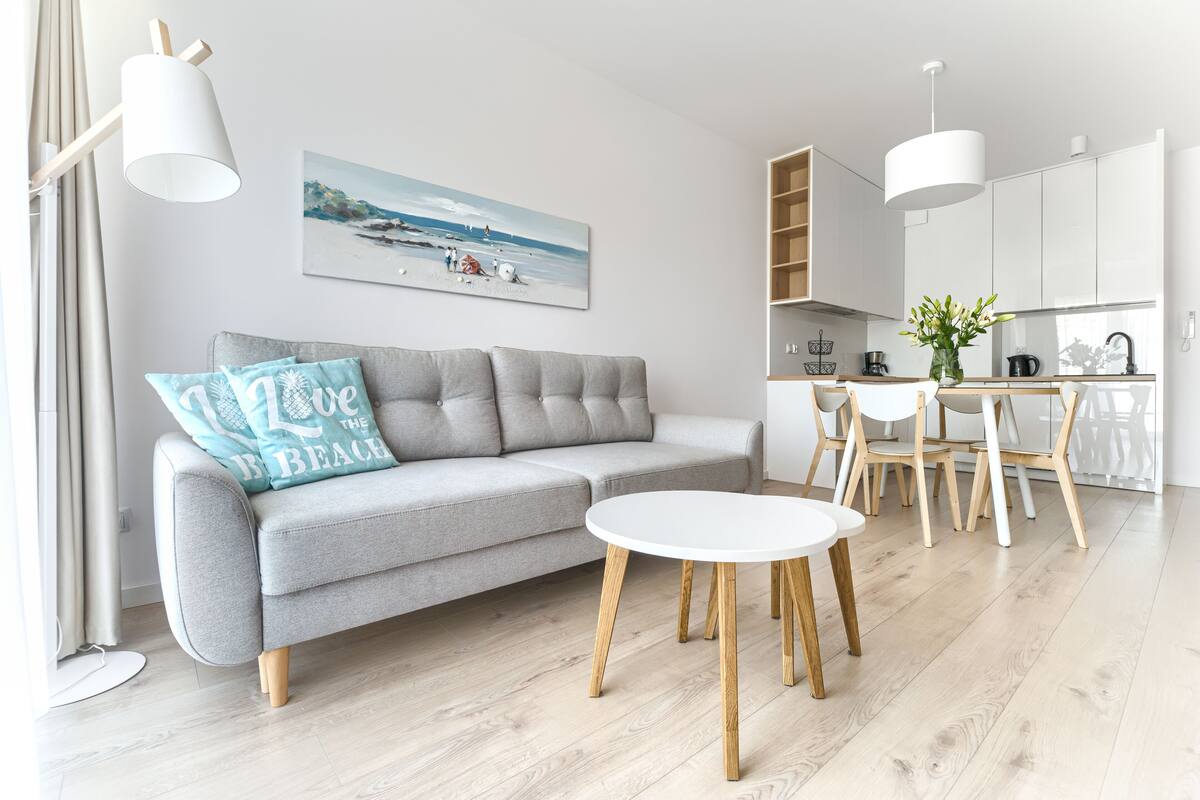 A modern living room with a grey sofa, a round coffee table, and a dining area with wooden chairs and a white table.