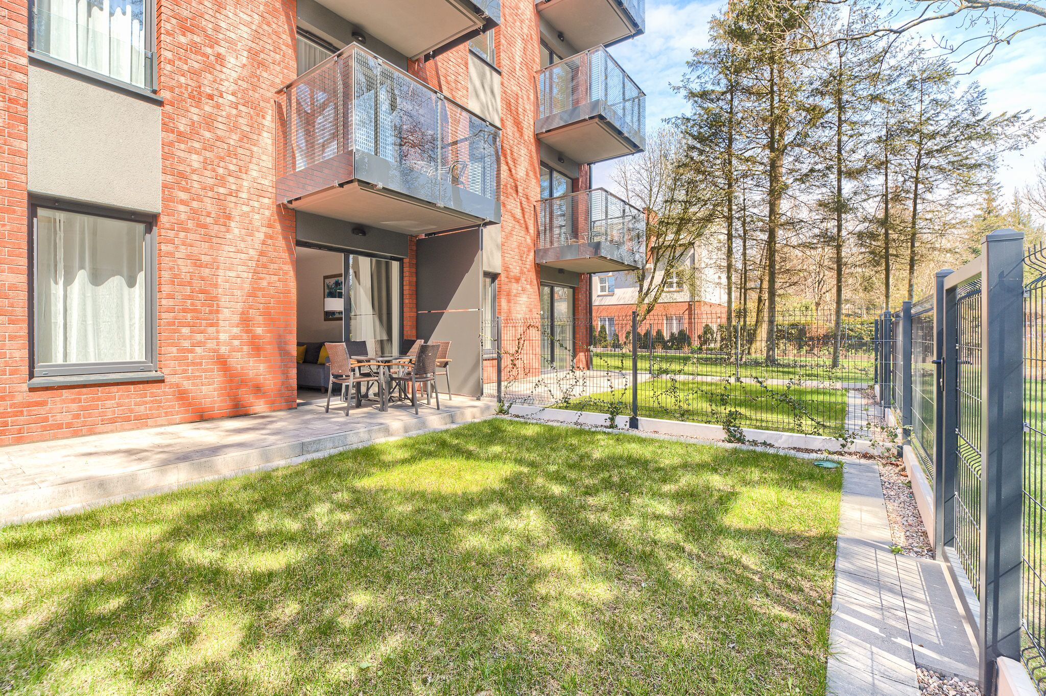A modern apartment building with a brick facade, large windows, and outdoor seating area.