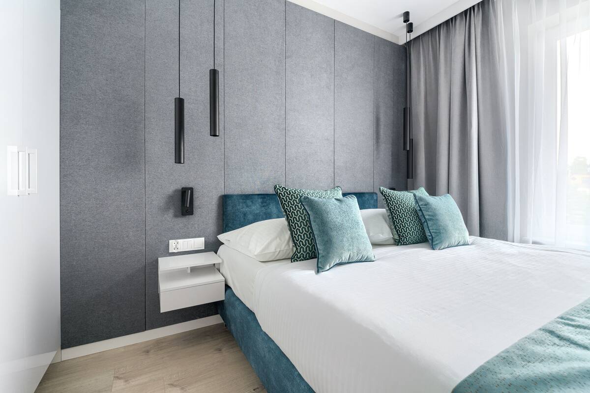 A modern bedroom with a large bed, grey textured walls, and a white nightstand.