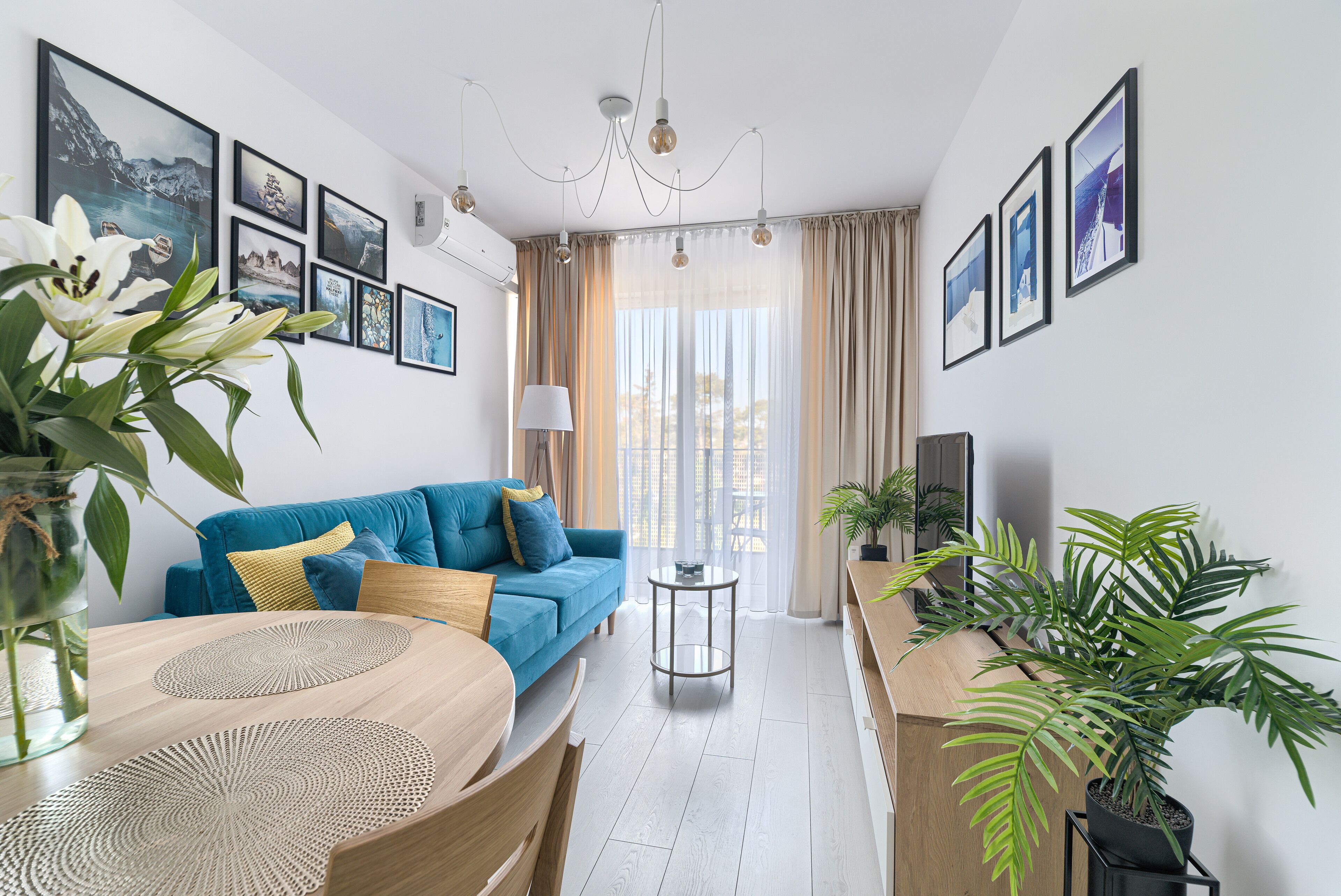 Una sala de estar moderna con un sofá azul, una mesa de comedor con individuales y una planta en maceta.