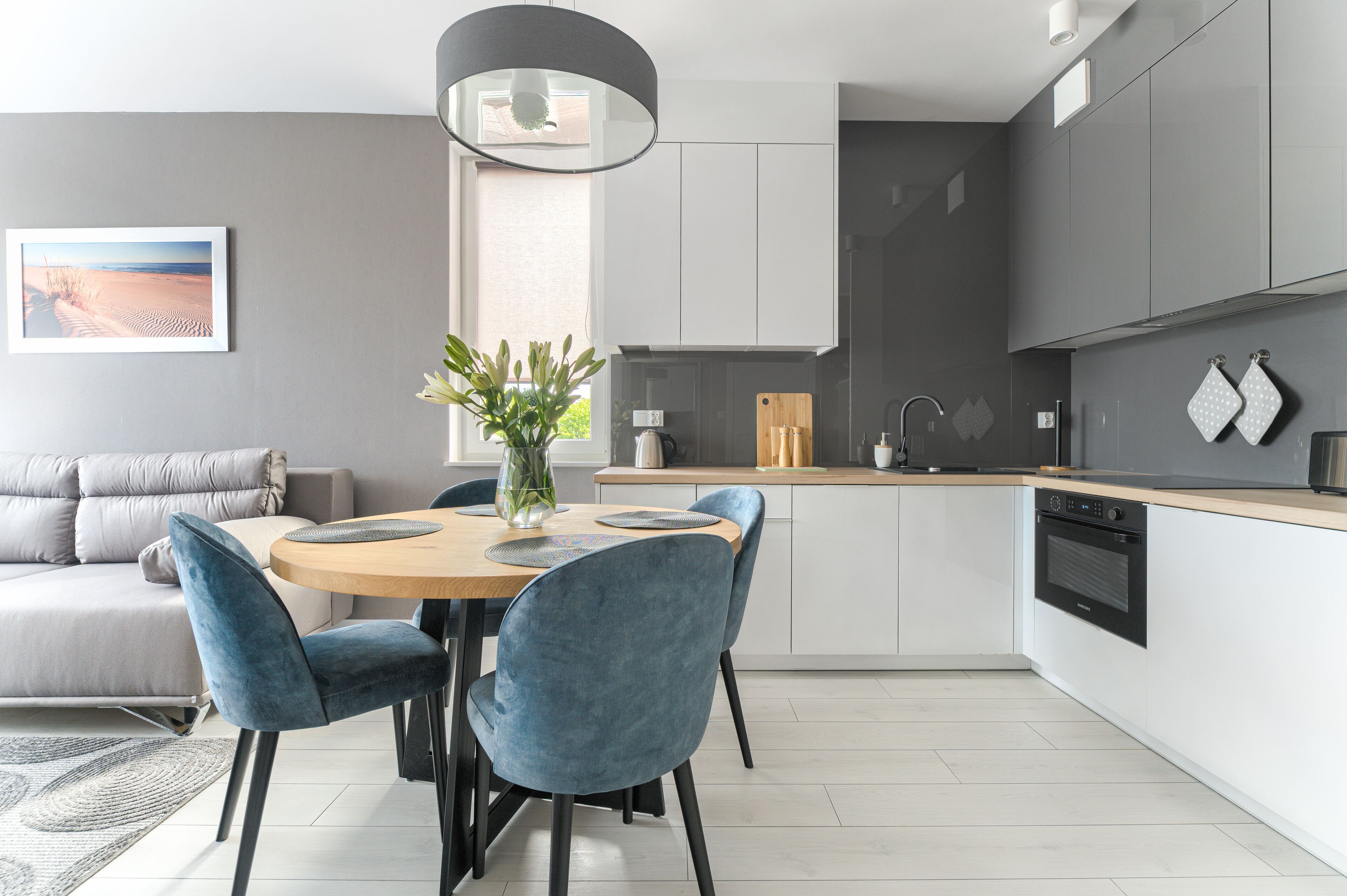 Eine moderne Küche mit grauen Schränken, einer Holz Arbeitsplatte und einem Essbereich mit einem runden Tisch und blauen Stühlen.