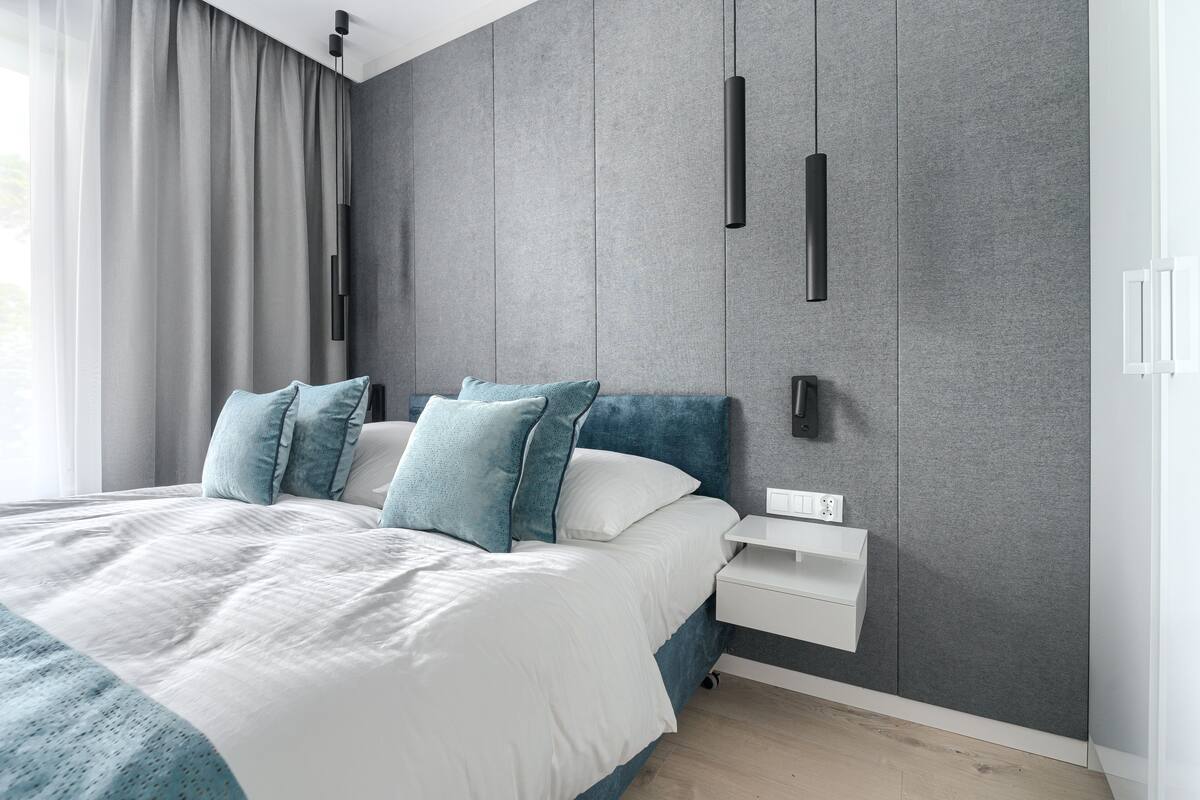 A modern bedroom with a bed, grey walls, and a white bedside table.