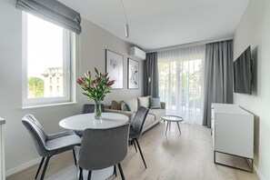 Un salon moderne comprenant un canapé, une table à manger avec des chaises, une petite table d’appoint et un téléviseur fixé au mur.