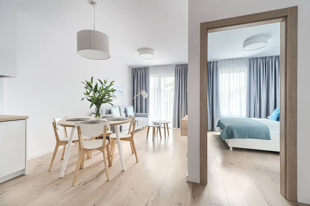 A modern, well-lit living area with a dining table, chairs, a sofa, and a bed.