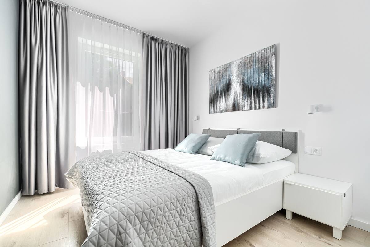A modern bedroom with a bed, bedside tables, and a large window with curtains.