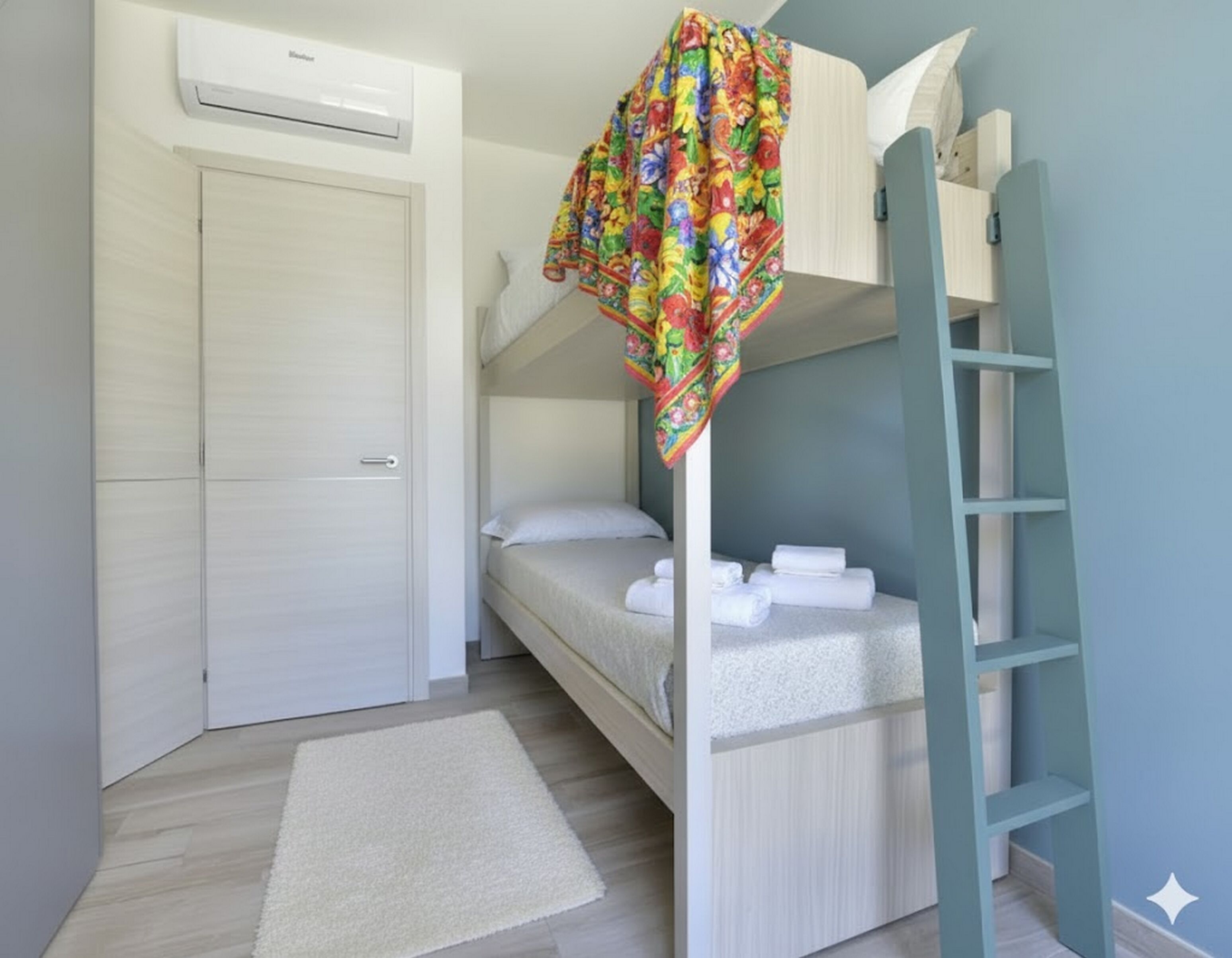 A bunk bed with a colorful canopy, a white door, and a small white rug on a wooden floor.