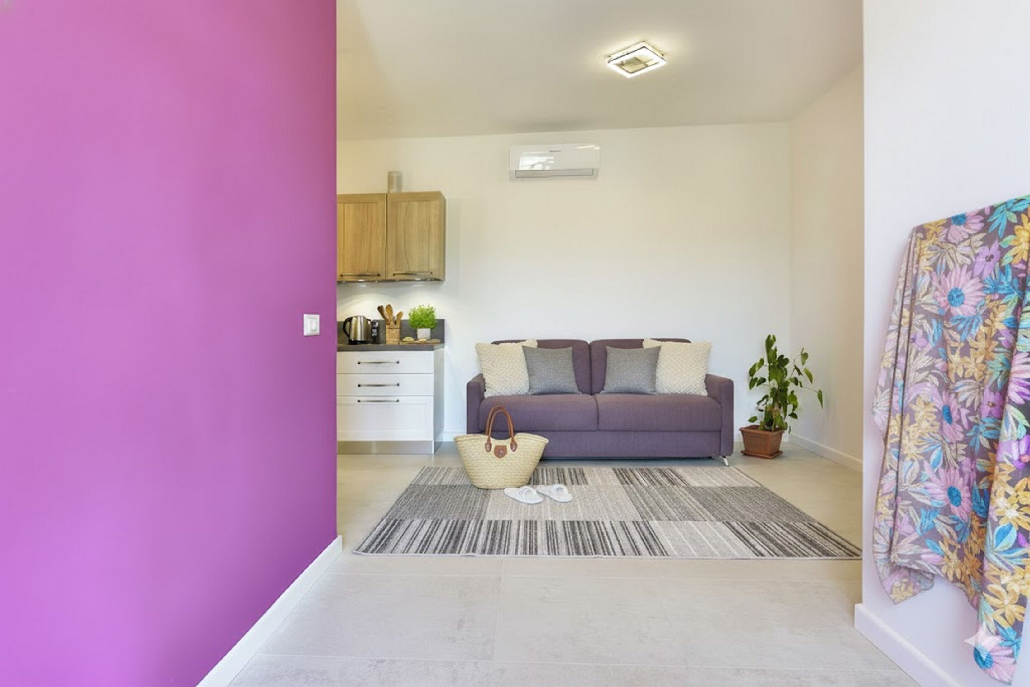 Een moderne woonkamer met een paarse bank, een gestreept tapijt en een keuken op de achtergrond.