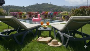 Zona de piscina con sillones de descanso, un flotador con forma de flamenco rosa y una mesa con bebidas y aperitivos.
