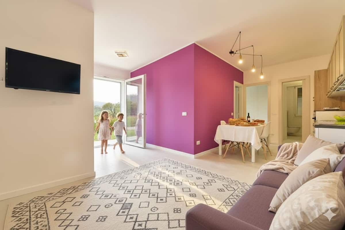 A modern living room with a purple accent wall, a flat-screen TV, a sofa, and a dining area with a table and chairs.