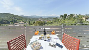 Una mesa al aire libre con una vista panorámica, una botella, vasos y un libro.