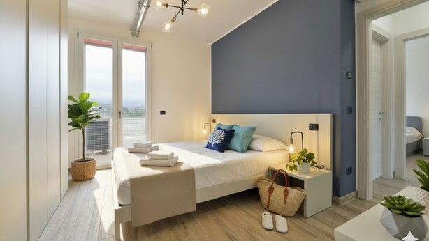 Un dormitorio moderno con una cama grande, mesitas de noche, una planta en maceta y vistas al exterior.