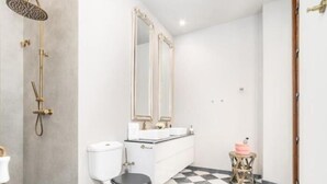 A bathroom with a checkered floor, a toilet, a sink with a mirror, and a shower with a gold showerhead. - iloftmalaga Luciano Martínez (Málaga)