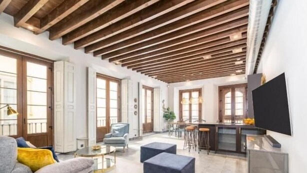 A spacious living area with a high ceiling, a sofa, ottoman, and a bar area with stools. - iloftmalaga Luciano Martínez (Málaga)